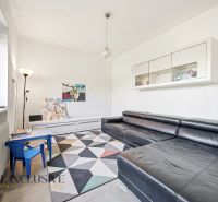 Living room with a black sofa, children's table, and geometric carpet in a family house.