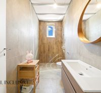 A bathroom in a family house with a wooden decor floor, a shower, and a round mirror.