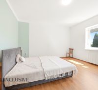 A bedroom in a family house with a light wall, a bed, and a wooden decor floor.