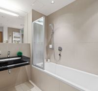A bathroom in a 2-room apartment with a bathtub, a sink, and a large mirror.