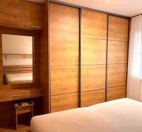 Bedroom with a large wardrobe and mirror, 2-room apartment with wooden decor flooring.