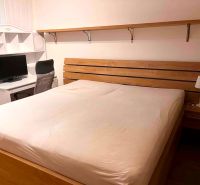Bedroom in a 2-room apartment with a bed, table, shelf, and desk lamp.