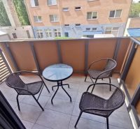 Balcony of a 2-room apartment with three chairs and a table, view of neighboring buildings.