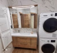 A bathroom in a 2-room apartment with a sink, washing machine, dryer, and a floor with a wooden decor.