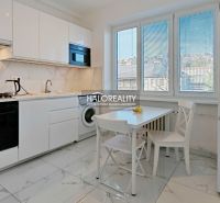 A bright kitchen in a 2-room apartment with white cabinets, a stove, and dining seating.