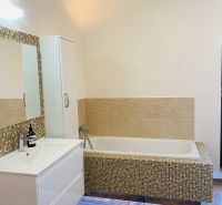 A bathroom in a family house with a bathtub, a sink, and a wooden decor floor.