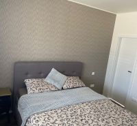 Bedroom in a family house with wallpaper, bed, and nightstand.