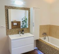 A bathroom in a family house with a mirror, a bathtub, and a floor with a wooden decor.