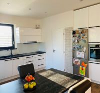 A kitchen in a family house with white cabinets, a dark table, and wooden decor flooring.