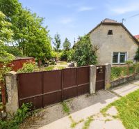 A family house in Lehnice with a gate and a garden, surrounded by greenery and a grassy area.
