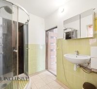 A bathroom with a corner shower, green tiles, a sink, and a mirror in a family house.