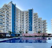 Residential complex in Iskele with a swimming pool, surrounded by tall buildings and palm trees.