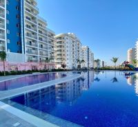 Apartment houses in Iskele with a swimming pool and palm trees in the area.