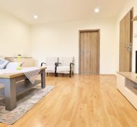 Living room of a three-room apartment with a wooden decor floor and light furniture.