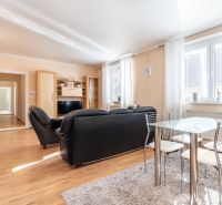 Living room in a 3-room apartment with a black sofa, glass table, and wooden decor flooring.
