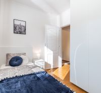A bright room in a 3-bedroom apartment with a bed and a wooden decor floor.