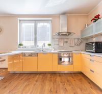 A bright kitchen with orange cabinets and a wood-patterned floor in a three-room apartment.