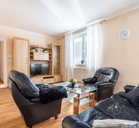 Living room in a three-room apartment with a black leather sofa and a wooden decor floor.