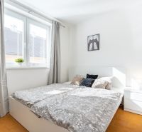 Bright bedroom with wood-patterned flooring in a 3-room apartment, light curtains, nightstand.
