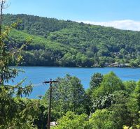 A view of the lake and surrounding hills from the cabin in Bukovec, surrounded by dense forest.