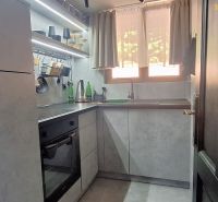 A kitchen in a cottage with a kitchen unit, shelves, and curtains.