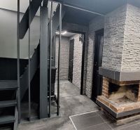 The interior of a cabin with a brick fireplace, staircase, and walls with stone cladding.