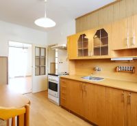 A kitchen in a 2-room apartment with light furniture and a wooden decor floor.