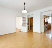 A room with a wooden floor design and entrances to the kitchen and another room.