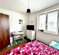 Bedroom with white furniture, colorful bed, and wooden decor flooring in a family house.