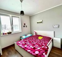 A bedroom in a family house with a wood-patterned floor, a white bed, and a pink blanket.