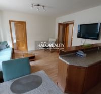 Living room in a three-room apartment with a sofa, television, and wooden decor flooring.