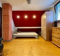 A bedroom in a family house with wooden flooring, a red wall, and furniture.