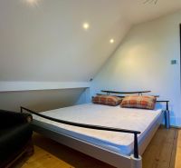 Bedroom with a bed and a chair in a family house, wooden floor, simple interior.
