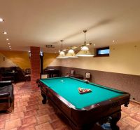 Interior of a family house with a billiard table, couch, and brick pillar.