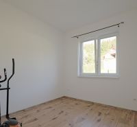 A room with a window, an exercise machine, and a wooden-decor floor in a family house.