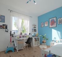 Children's room with a desk, blue wall, decorations, and wood-patterned flooring in a family house.