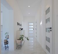 A bright hallway in a family house with plants and white doors on the tiles.
