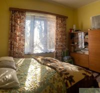 A room in a family house with a sunny window, a bed, and a wardrobe.