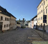 A street with historic buildings in the center of Štiavnické Bane, cobblestone pavement, and accessible parking.