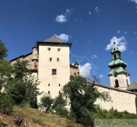 Historical architecture with a tower and a wall in Štiavnické Bane, surrounded by greenery and a blue sky.