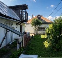 A garden with two buildings of a family house in Štiavnické Bane and a tree in the middle.