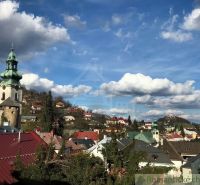 Panorama of Štiavnické Bane with the church tower, colorful roofs, and mountains in the background.