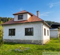 A family house in Štiavnické Bane with a lawn, trees, and forests in the background.