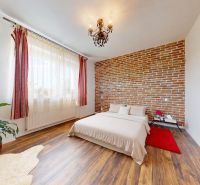 Bedroom with a brick wall, wood-patterned floor, plant, and chandelier.