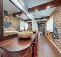 Bathroom in a family house with a brick wall, two sinks, wooden beams, and flooring.