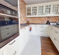 A kitchen in a family house with brick cladding and a wooden decor floor.