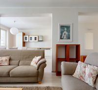 Living room with a sofa, wooden decor flooring, and a kitchen in a three-room apartment.