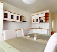 A kitchen with a dining table, white cabinets, wood-patterned flooring, 3-room apartment.