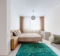 A bright bedroom of a 3-room apartment with a bed, green carpet, and a sofa.