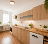 A kitchen in a 3-room apartment with a wooden decor floor and light cabinets.